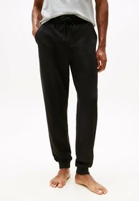 Pantalones de chándal negros hechos de una tela suave, con cintura elástica y cordón ajustable. Corte entallado con puños acanalados en los tobillos.