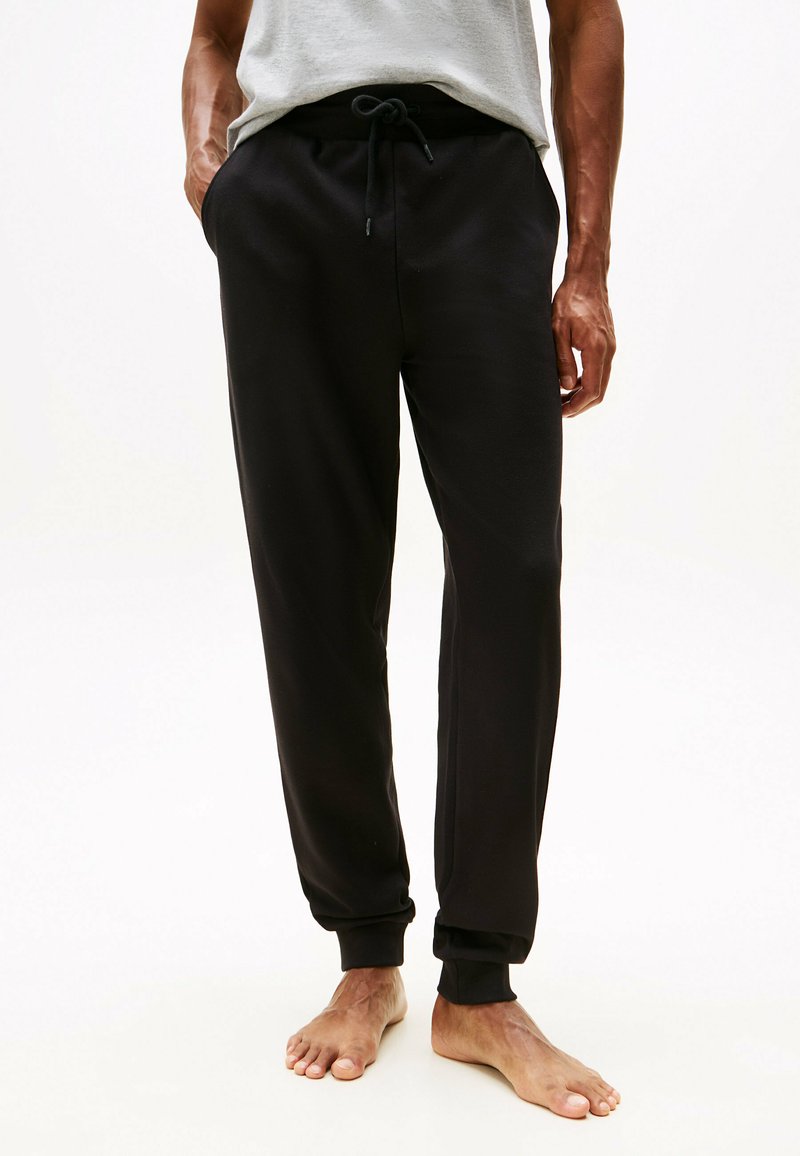 Pantalones de chándal negros hechos de una tela suave, con cintura elástica y cordón ajustable. Corte entallado con puños acanalados en los tobillos.
