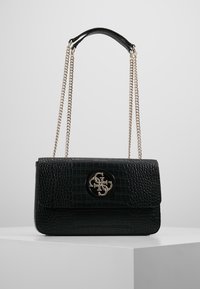 Černá kabelka z umělé krokodýlí kůže s klopou a zlatým kováním. Má řetízkový popruh a kruhový akcent s logem.