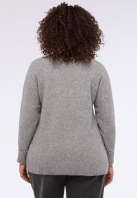 Suéter gris hecho de un material suave, con un dobladillo acanalado y detalles de cadena en los puños. La vista trasera muestra un ajuste relajado y una textura suave.