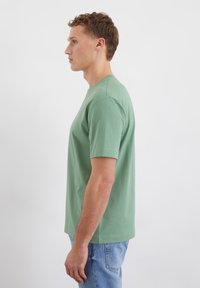 T-shirt a maniche corte di un verde chiaro in vestibilità rilassata. Realizzato in morbido cotone con scollatura rotonda. Nessun motivo visibile o dettagli in metallo.