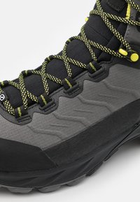 Czarne i szare buty trekkingowe z teksturowaną cholewką, żółtymi sznurowadłami i gumową podeszwą, z zygzakowymi wzorami i wzmocnionym czubkiem.