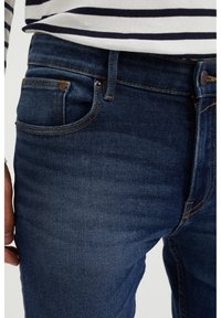 Mörkblå denimjeans med en klassisk design, synliga sömnadsdetaljer, subtil blekning och en metallknapp som stängning i midjan.