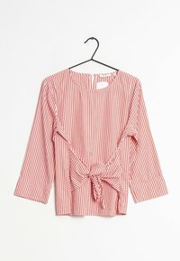 Červeno-bíle pruhovaná blůza s tříčtvrtečními rukávy, kulatým výstřihem a detailem uvázání vpředu, zavěšená na černém ramínku.