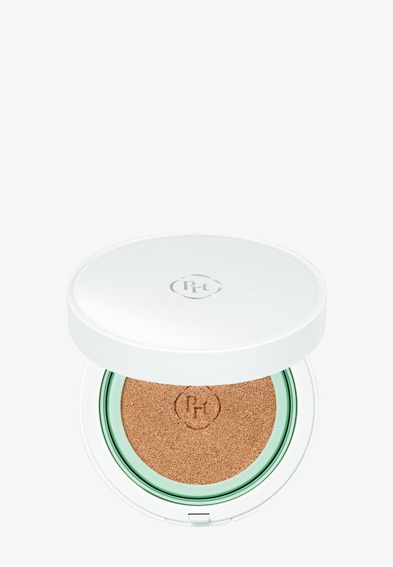 Fond de teint cushion compact avec un couvercle blanc et une éponge beige visible à l’intérieur, marqué d’un logo circulaire sur le couvercle et l’éponge.