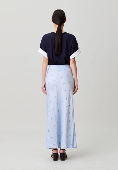 Camicia a maniche corte blu navy con dettagli bianchi sui polsini, abbinata a una maxi gonna azzurra con motivo floreale. Sandali neri con tacco spesso.