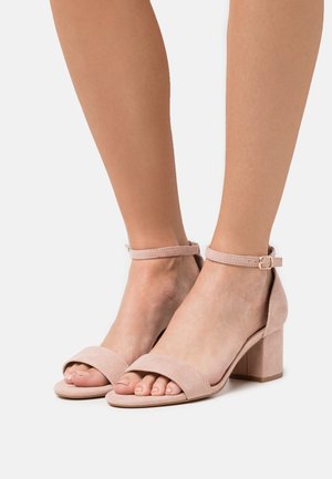 Helle rosa Wildleder-Absatzsandalen mit einem Knöchelriemen, offener Zehenpartie und Blockabsätzen. Glatte Textur und minimalistischem Stil.