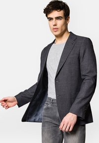 Czarna szara marynarka z teksturowanej tkaniny, na dwa guziki, z podszewką w groszki. Połączona z jasnoszarym t-shirtem i dżinsami.