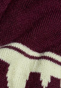 Stickad tröjfabric i mörk bourgogne med kontrasterande krämfärgad zigzagmönster; visar textur och lager av garn för en mysig känsla.