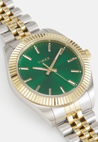 Orologio Timex con quadrante verde, accenti dorati, cassa in acciaio inossidabile argentato e bracciale metallico bicolore. Presenta una lunetta testurizzata e marker.