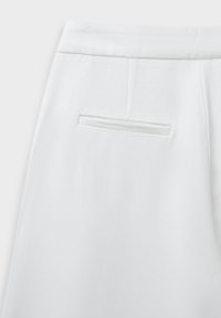 Pantalon en tissu blanc avec une poche arrière à fente, texture lisse et coupe épurée avec des détails de couture minimes.