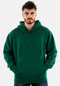 Felpa verde realizzata in tessuto morbido, con tasca a marsupio frontale e logo in rilievo sul petto. Vestibilità casual con cappuccio regolabile.