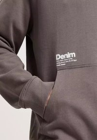 Szary bawełnowy sweatshirt z kieszenią z przodu, ściągaczami przy rękawach i białym napisem "Denim" nadrukowanym w dolnym lewym rogu.