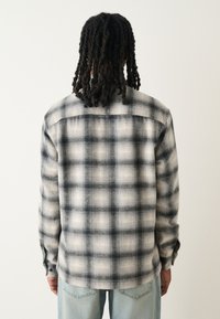 Camicia di flanella a quadri neri e bianchi con vestibilità rilassata, maniche lunghe e collo con bottoni. Tessuto morbido con cuciture visibili.