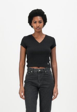 Top cropped noir près du corps en V, fait de tissu doux, associé à un jean foncé à taille haute. Remarqué pour ses manches courtes et son logo subtil.