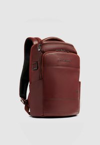 Sac à dos en cuir rouge avec dos rembourré, plusieurs compartiments zippés et une poche latérale. Design épuré avec détails de marque.