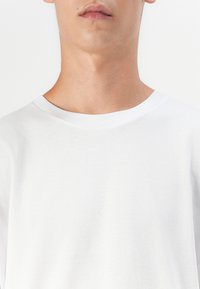 Hvid bomulds T-shirt med en klassisk rund hals. Blød tekstur, korte ærmer og et simpelt, rent design uden mønstre eller accenter.