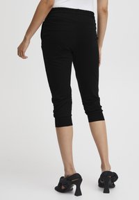 Černé, zkrácené kalhoty s elastickým pasem a přiléhavými manžetami. Hladká tkanina, obsahující boční kapsy. V kombinaci s černými sandály na podpatku.