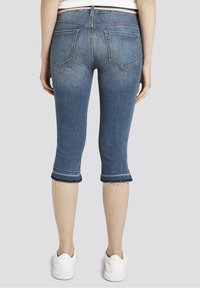 Pantalones capri de mezclilla, tono azul, de cintura media, estilo de cinco bolsillos, con dobladillo deshilachado, longitud recortada, textura suave, combinados con zapatillas blancas.