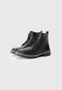 Bottines en cuir noir avec une finition texturée, dotées d'œillets en métal, d'un lacet, et d'une semelle en caoutchouc marron contrastante.