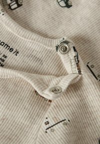 Geribbelde beige babyromper met drukknoopsluiting, met kleine bedrukte ontwerpen in donkergroen en bruin. Zachte stof met een gestructureerd gevoel.