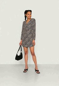 Vestido mini preto com padrão floral, mangas longas, decote em V, tecido leve e silhueta ajustada. Combinado com uma bolsa preta e sandálias de salto.