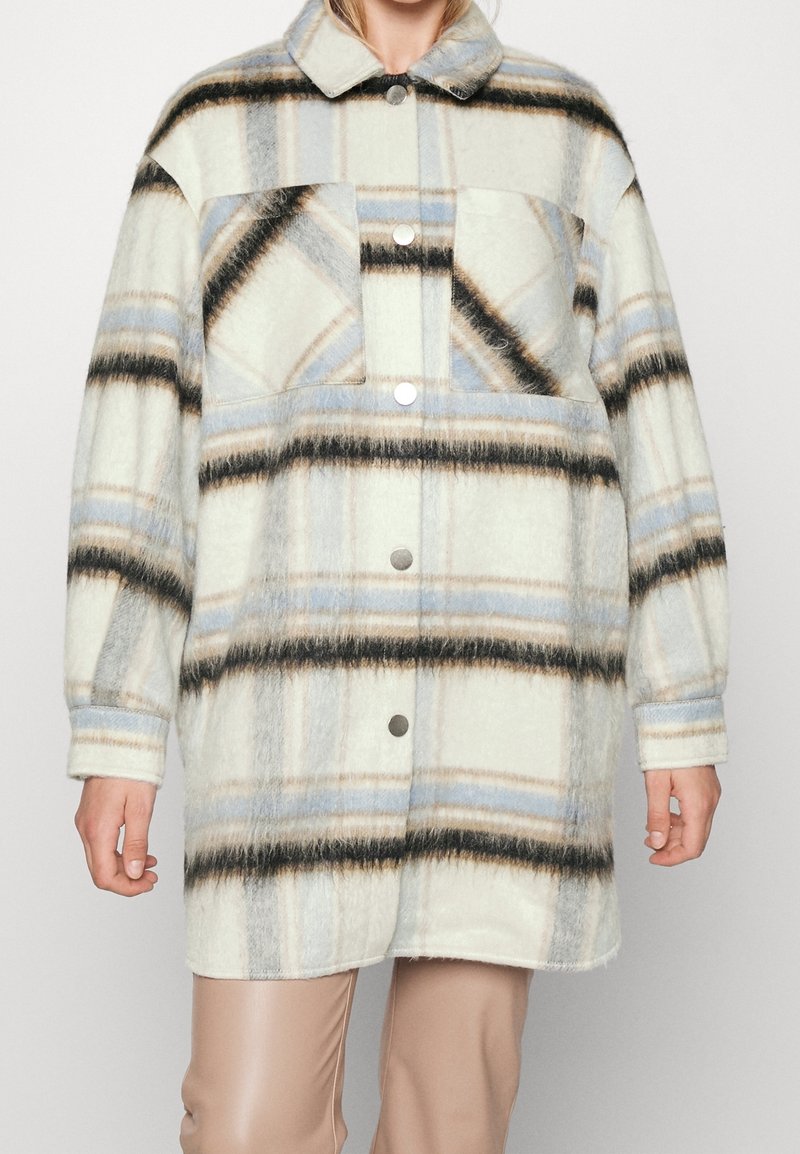 Abrigo a cuadros con una textura similar a la lana en blanco, azul y negro. Tiene un cuello, cierres de botones y dos bolsillos frontales.