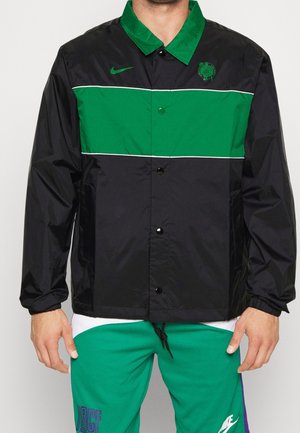 Chaqueta cortavientos negra con rayas horizontales verdes y blancas, cierre de botones y logotipo bordado en el pecho. Textura suave.