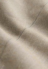 Beige textured fabric with a smooth, woven surface, featuring fine diagonal lines and subtle stitching details.