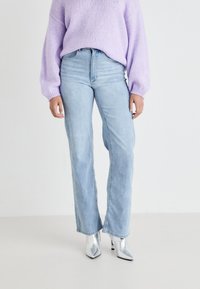 Jeans de perna larga azul claro, combinados com um suéter de malha lavanda, com mangas bufantes e botas prateadas de salto alto. Textura suave.
