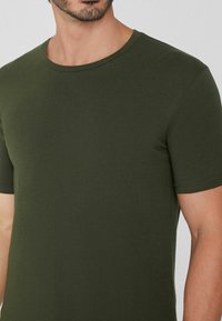 Oliwkowy t-shirt z krótkim rękawem wykonany z gładkiej bawełny, z okrągłym dekoltem i czystymi, prostymi szwami. Brak widocznych logo lub wzorów.