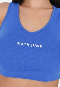 Crop top blu ribbed con scollatura a V e testo bianco che dice "SIXTH JUNE" sul petto. Texture liscia, design aderente.