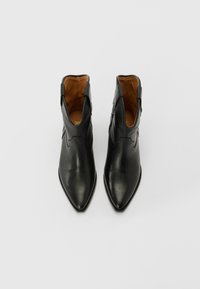 Botines de cuero negro hasta el tobillo con puntera afilada, que presentan una textura suave, un detalle de costura mínima y un forro interior en color marrón claro.