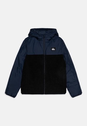 Doudoune avec une partie supérieure bleue marine et une partie inférieure en polaire noire, dotée d'une capuche et d'une fermeture éclair à l'avant ; comprend un patch logo sur la poitrine.