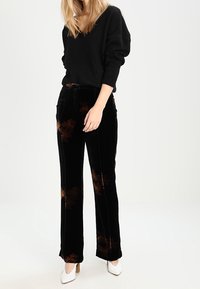 Zwarte fluwelen broek met bruine palmbladpatroon, gecombineerd met een zwarte v-hals trui met lange mouwen en een ontspannen pasvorm.