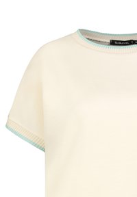 Helle Creme T-Shirt mit kurzen Ärmeln und rundem Ausschnitt. Ausgestattet mit einem türkisfarbenen Rippkragen und -bündchen. Weicher Stofftextur.