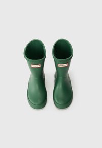 Botas de chuva infantis verdes de borracha com uma textura suave, forma arredondada e um rótulo com logo na frente. Solas ligeiramente texturizadas para maior aderência.