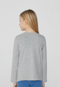 Dlouhý rukáv šedého trička z měkké, melanžové látky s kulatým výstřihem a volným střihem, nošeného s modrými džíny.