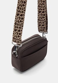Bruine faux leren crossbody tas met zilveren rits. Heeft een gestructureerde beige strap met een bruine panterprint. Compact rechthoekige vorm.