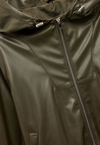 Veste à capuche en cuir vert olive avec des détails en métal argenté, dotée d'un zip à l'avant et de coutures en biais, texture lisse et poches latérales.