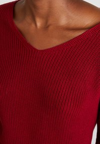 Rode geribbelde trui met een V-hals, textuur gebreide stof, met gedetailleerd stikwerk en een gelijkmatig verdeeld patroon over het geheel.