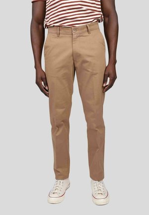 Pantalon en coton beige avec une coupe droite, fermeture à crochet et à glissière, associé à des baskets blanches. Chemise rayée visible au-dessus.