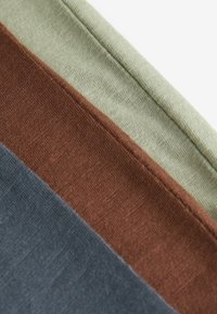 Tissu en coton présentant trois bandes horizontales : bleu foncé, marron et vert clair. Surface texturée avec des coutures visibles le long des bords.