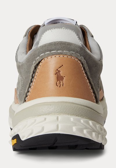 Vue arrière d'une basket grise et beige avec une semelle texturée et un logo de joueur de polo embossé sur le contrefort du talon.