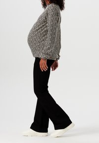 Blusa a fantasia bianco e nero con maniche lunghe, indossata sopra pantaloni neri a zampa d'elefante e sneakers bianche, che mette in risalto una forma evidente della pancia.