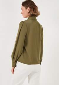 Olive green blouse with long puffed sleeves, a high collar, and buttoned cuffs. Smooth texture and slightly draped fit.