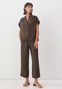 Haut marron à manches courtes avec un col en V, associé à un pantalon large assorti. Le tissu a une apparence douce et texturée. Sandales à fines brides.