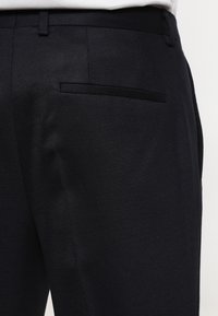 Svarta texturerade byxor har en smal passform, med en enda bakficka och ett stilrent midjeband. Tyget har ett subtilt mönster för extra detalj.