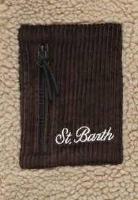 Tasca con zip in velluto a costine marrone su uno sfondo beige soffice, con testo ricamato bianco "St. Barth" nell'angolo in basso a destra.