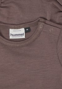 Braunes Baumwollshirt mit rundem Ausschnitt, ausgestattet mit Druckknöpfen an der Schulter und einem Etikett mit der Aufschrift "hummel" zur Markenidentifikation.